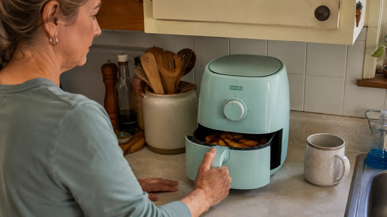 Hand pulling out the round basket from the compact Dash Tasti-Crisp air fryer on a countertop