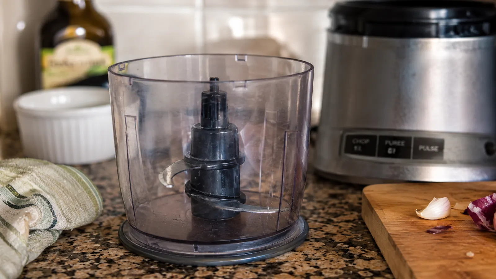 Close-up of the small stainless steel blade and scratched plastic bowl of the chopper sitting empty on a counter