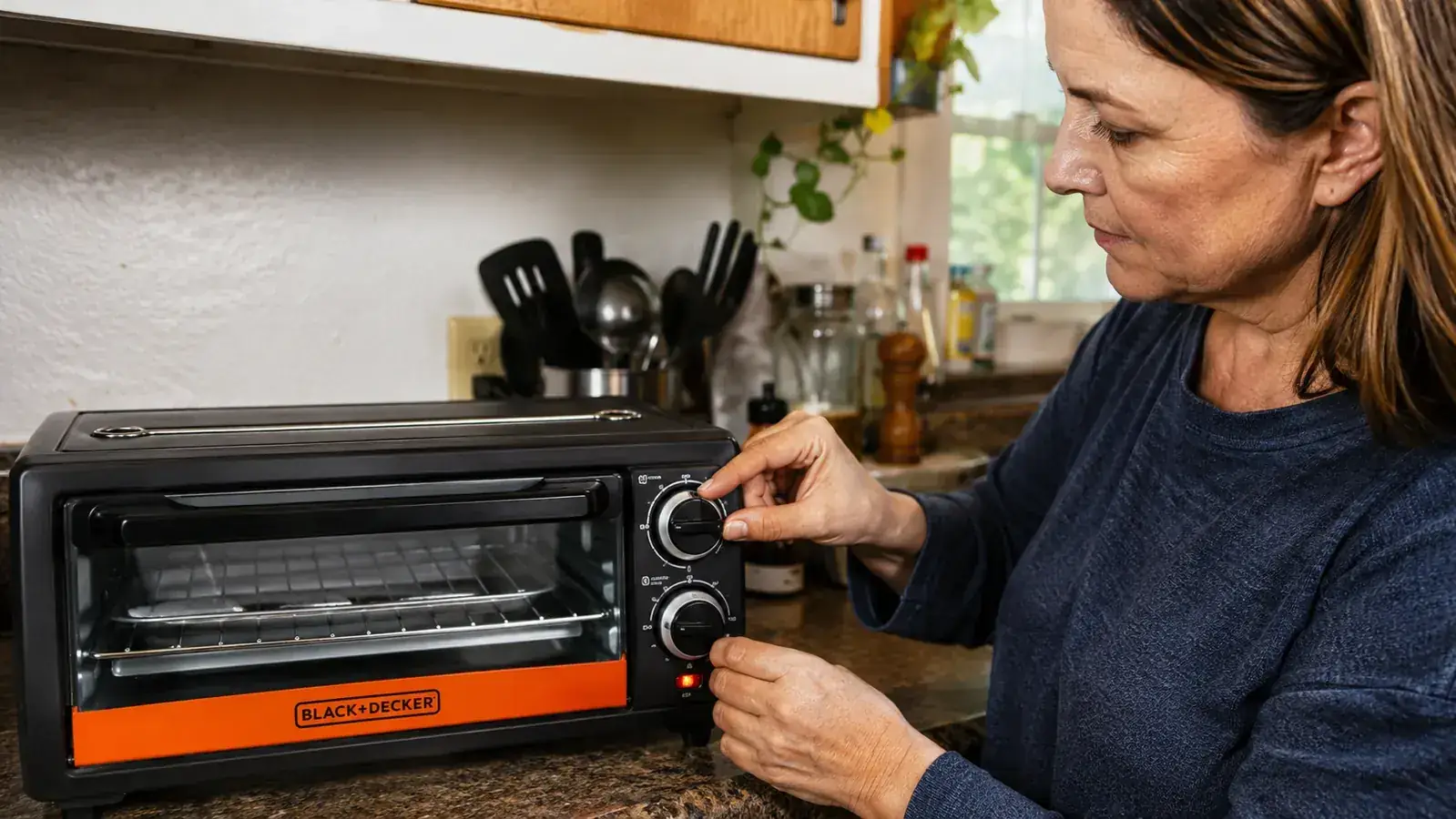 Hand turning the toast shade dial on the front of the BLACK+DECKER toaster oven before starting a batch