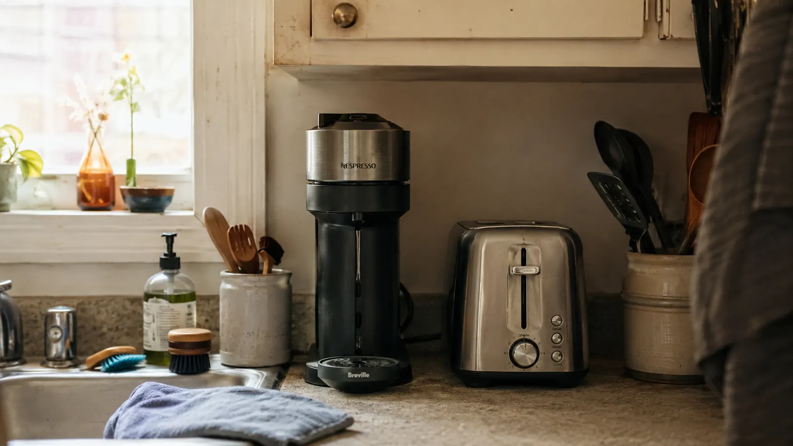 Slim black single-serve coffee maker tucked into a narrow gap between a toaster and the wall in a small kitchen