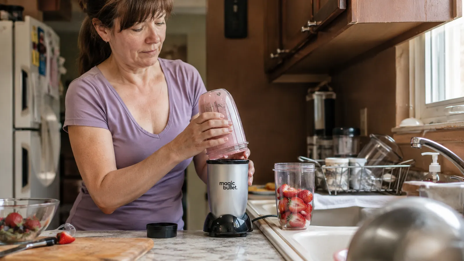 Hand lifting the cup off the Magic Bullet blender base after blending a smoothie